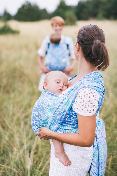 ruky rodiča držia novorodenca v ergonomickom nosiči