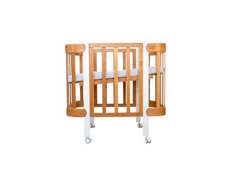 Detská postieľka s dreveným rámom a bielymi prútnicami.