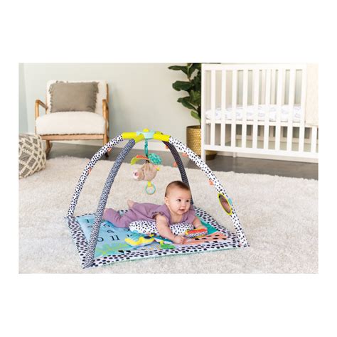 Dieťa hrajúce sa na farebnej hracej deke s hrazdou a zavesenými hračkami